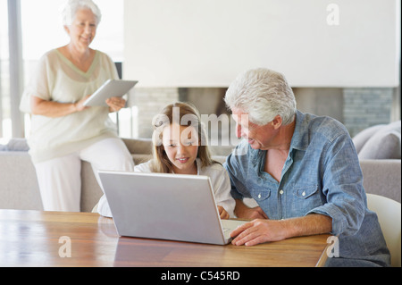 Man using a laptop with his granddaughter and his wife working on a digital tablet in background Stock Photo