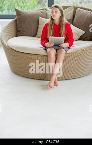 Girl sitting in a wicker couch using a digital tablet Stock Photo