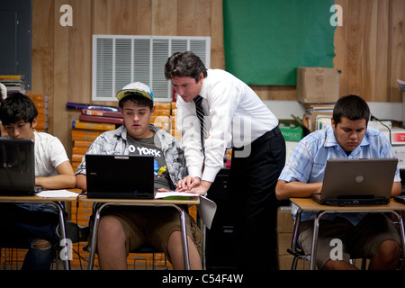 Young Hispanic male teacher helps Hispanic male student using laptop computer on desk in high school classroom in El Paso, Texas Stock Photo