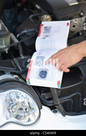 Close-up of a human hand pointing at book while working on broken car engine Stock Photo