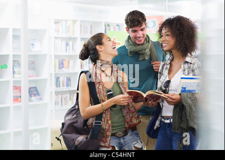 University students smiling while reading a book in a library Stock Photo
