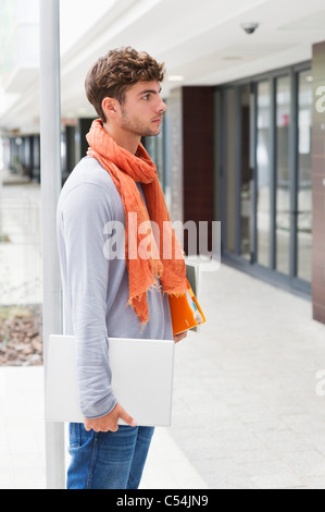 Side profile of a man standing with books and laptop in hands Stock Photo