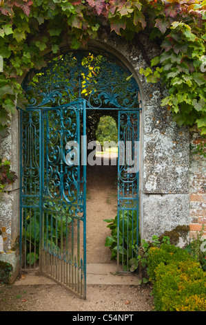 Ornate wrought-iron gate set in a Cotswold stone arch framed by vine leaves. Looking out of the walled garden at Rousham House, Oxfordshire, England Stock Photo