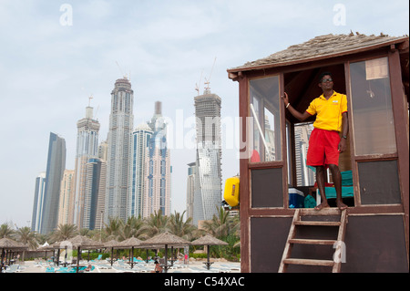 Hotel lifeguard on duty at Jumeirah Beach with high rise buildings at Dubai Marina to rear in Dubai United Arab Emirates Stock Photo