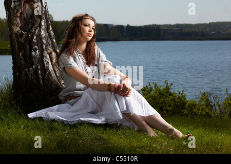outdoor portrait of beautiful hippie girl sitting near birch. lake and forest on background Stock Photo