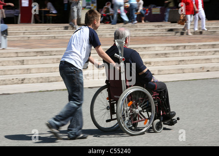 Old man in a wheelchair pushed by a boy, Berlin, Germany Stock Photo
