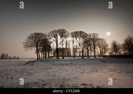 The Netherlands, Hijum, Church on mound in snow at sunrise. Stock Photo