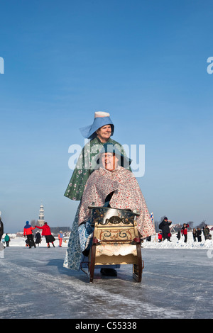 The Netherlands, Hindeloopen, Dutch capital of skating culture. Women dressed in traditional costume with sledge on ice. Stock Photo