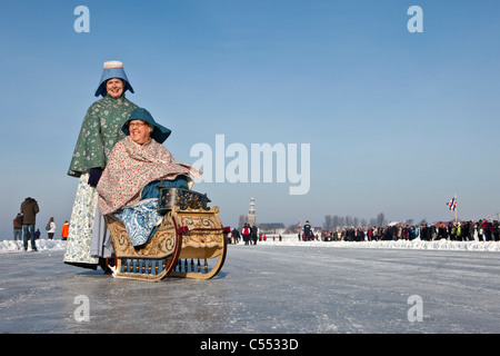 The Netherlands, Hindeloopen, Dutch capital of skating culture. Women dressed in traditional costume with sledge on ice. Stock Photo