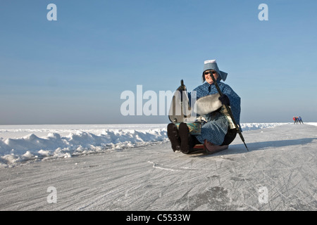 The Netherlands, Hindeloopen, Dutch capital of skating culture. Woman dressed in traditional costume. Sledge moved by prickers. Stock Photo