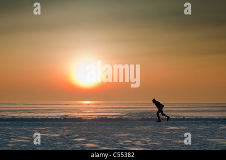 The Netherlands, Hindeloopen, Ice skater on lake called IJsselmeer at sunset. Stock Photo