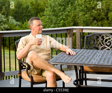 Man drinking beer sitting on a deck in the garden / back yard, USA Stock Photo