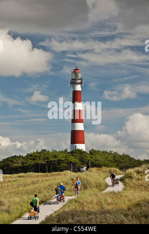 The Netherlands, Hollum, Ameland Island. People on bicycle on beach road. Lighthouse. Stock Photo