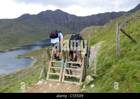 Walkers climbing over wooden stile on the Pyg Track, Snowdonia National Park Wales UK Stock Photo