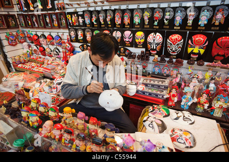 Artist painting Chinese masks in a store, Silk Market, Beijing, China Stock Photo