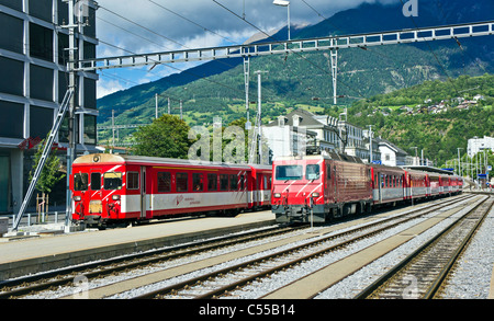 Two Matterhorn Gotthard Bahn trains at Brig Railway Station in Brig Switzerland with the train on left leaving towards Visp Stock Photo