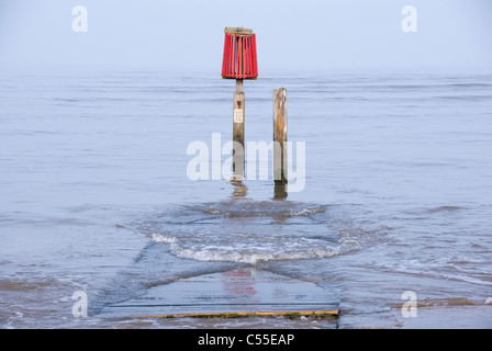 Red Warning Marker & Gentle Waves Lapping Over Wooden Jetty as Tide Comes In, Cleethorpes, South Humberside, UK Stock Photo
