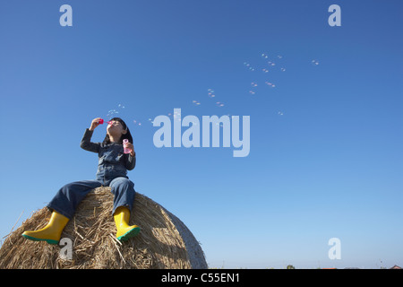 A girl sitting on a hay bale blowing soup bubbles Stock Photo