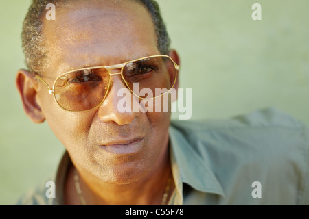 portrait of mature hispanic man with sunglasses looking at camera against green wall with serious expression. Copy space Stock Photo