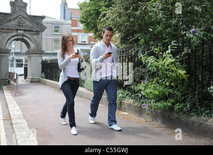 Young couple walking along the street using their IPhone mobile phones (posed by models) Stock Photo