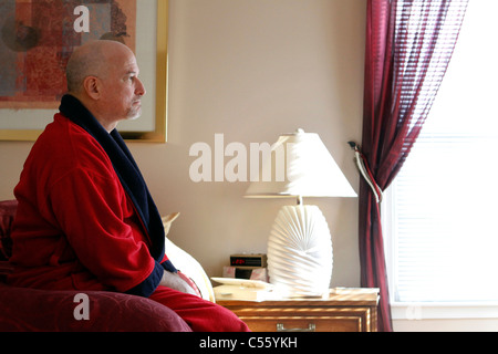 Mature man sitting on bed looking serious Stock Photo