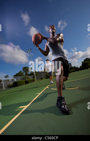 males playing outdoor basketball game, one driving to basket Stock Photo