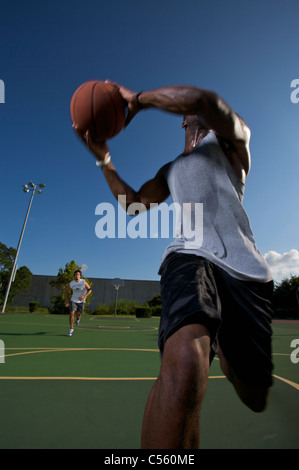 males playing outdoor street basketball with one player driving to basket Stock Photo