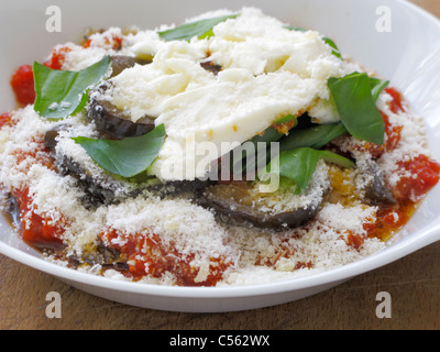 melanzane alla parmigiana individual portion in a white dish on of a wooden table kitchen chopping board prepared ready for oven Stock Photo