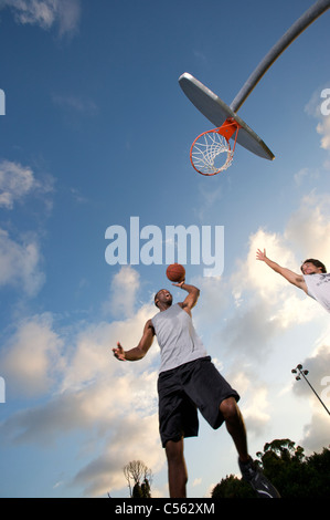 male scoring during outdoor basketball game, looking upward toward goal Stock Photo