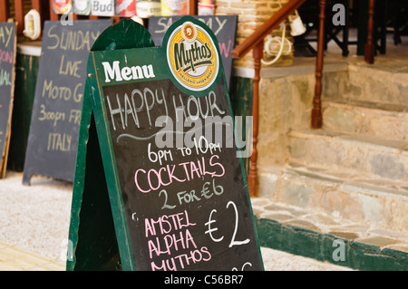 Sign outside a Greek bar advertising Happy Hour from 6pm to 10pm with cheap cocktails and beer Stock Photo