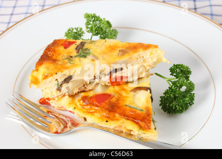 Two pieces of home-made spanish omelet on a plate with a fork and garnished with parsley Stock Photo