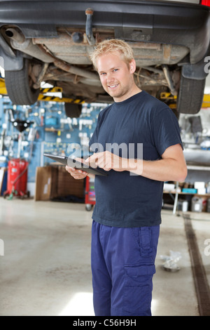 Portrait of young mechanic standing and using digital tablet in his auto repair shop Stock Photo