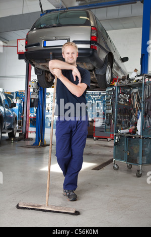 Full length portrait of young man leaning on broom in garage Stock Photo