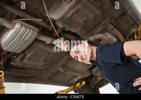 Low angle view of smiling young female mechanic repairing car in auto repair shop Stock Photo