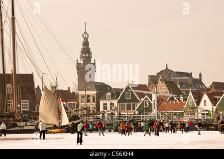 The Netherlands, Monnickendam, skyline of village. People ice skating on frozen lake called Gouwzee. Left ice sailing boat. Stock Photo