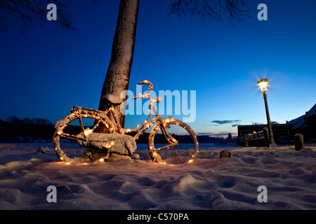 The Netherlands, 's-Graveland, bicycle decorated with Christmas lights in snow. Dawn. Stock Photo