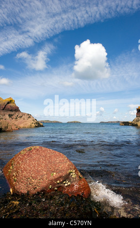 Waves gently breaking against a limpet covered red rock at North Haven Skokholm Island Pembrokeshire South Wales UK Stock Photo