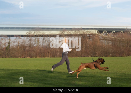 Woman running with dog in field Stock Photo