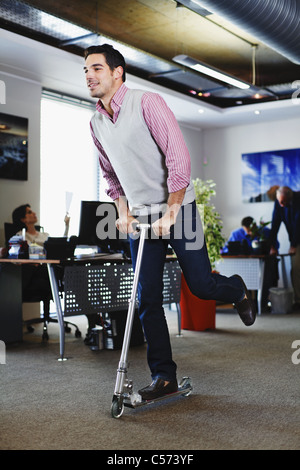 Businessman riding scooter in office Stock Photo