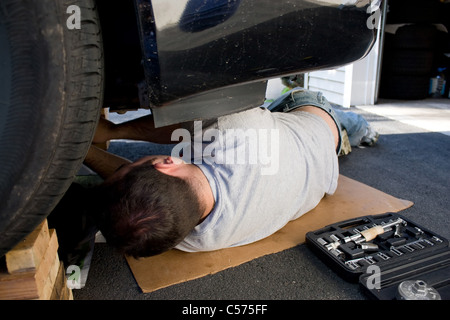A young man laying underneath a car doing repairs or maintenance on the vehicle. Stock Photo