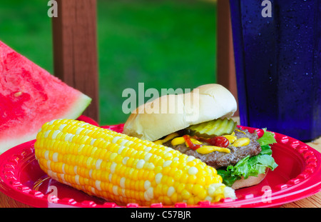 Summer picnic fare - hamburger, sweetcorn, and watermelon - in an outdoor setting Stock Photo