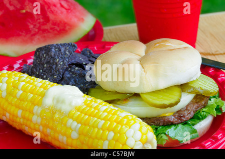Summer picnic meal - hamburger, buttered sweetcorn, chips, and watermelon - in an outdoor setting Stock Photo