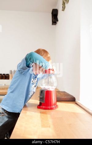 Boy opening gum ball machine in kitchen