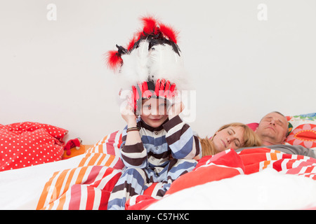 Boy wearing war bonnet in parents’ bed Stock Photo