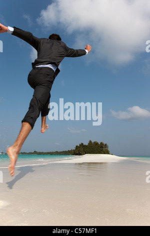 Businessman jumping on tropical beach Stock Photo