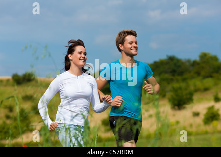 Young fitness couple doing sports outdoors; jogging on a green meadow in summer under a blue sky Stock Photo