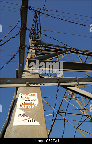 Close-up shot looking up from the base of a hydro-tower with barbed wire and warning sign. Stock Photo