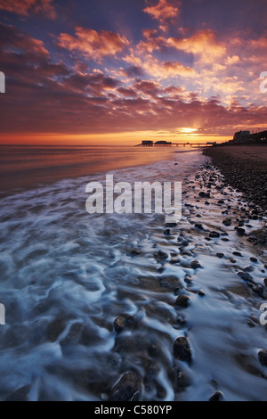 Looking along the shoreline at the sunrise behind Cromer pier on the Norfolk coast Stock Photo