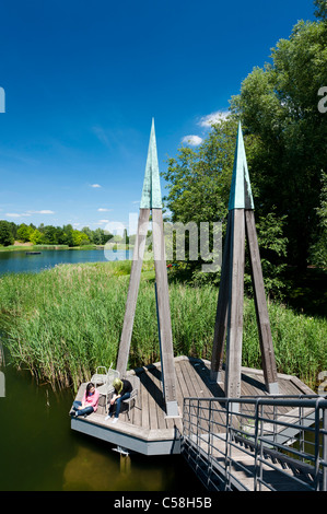 Visitors sitting on wooden footbridge crossing lake at Britzer Garden in Neukolln in Berlin Germany Stock Photo