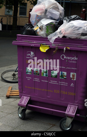 A wheelie bin overflowing with rubbish with part of a dumped bicycle nearby Stock Photo